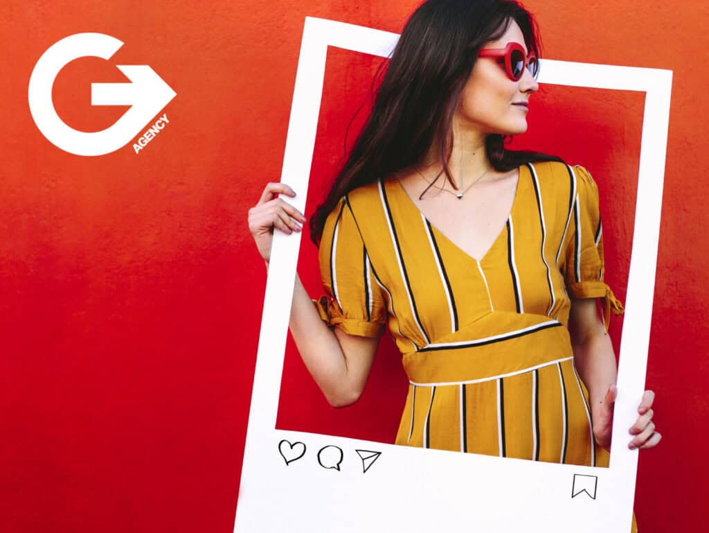 Stylish woman holding a large Instagram photo frame against a red background with G Agency logo.